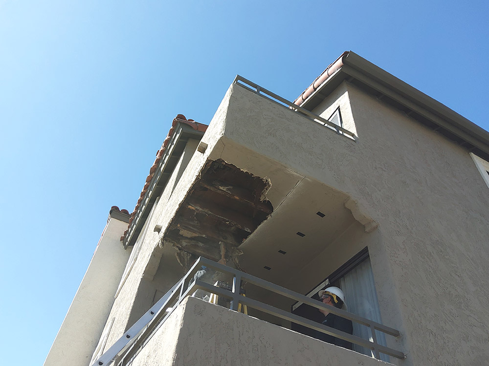 Underside of closed soffit balcony with stucco removed to reveal rotting wood in need of SB721 compliant repairs