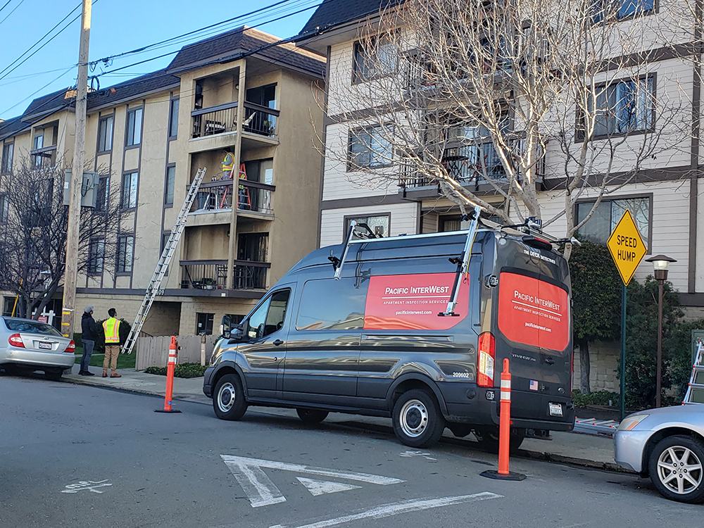 PIW Apartment Inspection Services van parked outside a residential community with inspectors working on nearby balconies